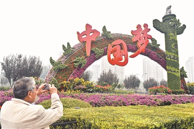 2013年9月30日，一名行人在北京復(fù)興門橋拍攝“中國夢”主題花壇。（資料圖片）